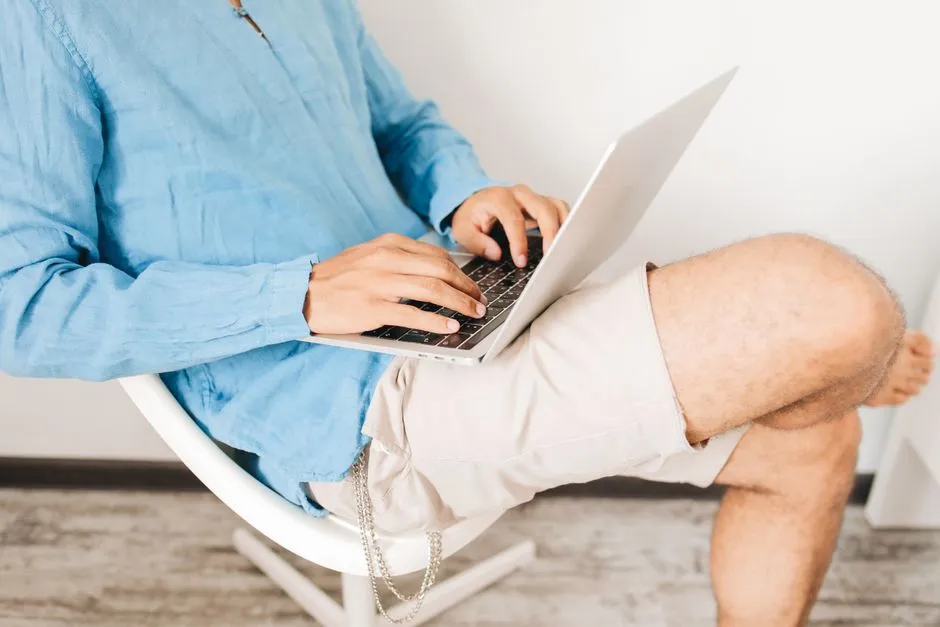 Someone typing a short message on a laptop at a kitchen table with a notebook open beside them